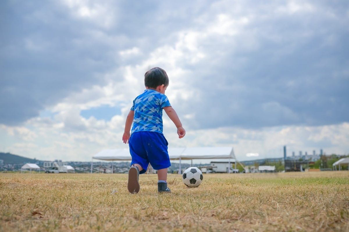 football, child, kick, meadow, playing, leisure, running, boy, playground, artificial grass, cloudless, blue clothing, child's play, outdoor activities, shoe, nature, clouds, joy, fun, childhood, natural environment