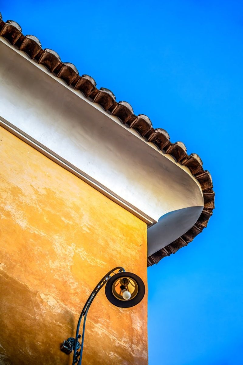 facade, architecture, lamp, outdoor lighting, blue sky, yellow, ornamentation, corner, light, aesthetic, edge, corner decoration, vertical lines, height details, yellow-orange facade, ornamental corner, outdoor architecture, classic style, aesthetic facade