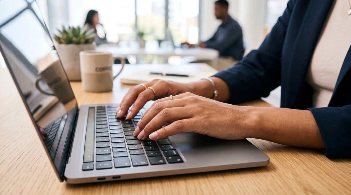 laptop, typing, hands, woman, office, desk, workspace, work desk, office environment, business, coffee mug, plant, close-up, employee, professional, technology, modern, nature, digital, multitasking, industry