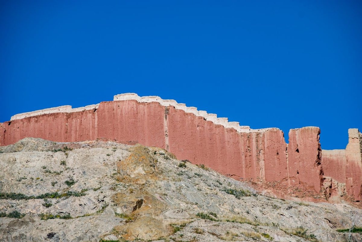 gyantse dzong, tibetan fortress, rammed earth wall, red ancient wall, historical ruins, bright blue sky, old fortress, architectural landmark, shigatse, ruins, exterior, stone cliff, angle from below, tourist attraction, ancient architecture, tibetan culture, terracotta color, expansive view, serene