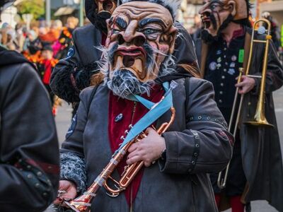carnival, musician, trumpet, trombone, wooden mask, black coat, beard, fake mustache, costume, parade, region, traditional, public event, band, festival, colorful, face paint, outdoor event, vibrant festival