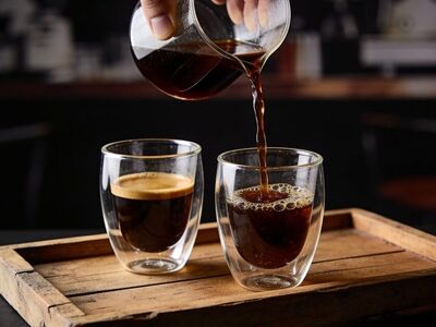 hand, black coffee, glass server, coffee crema, pouring, hot beverage, double-walled glass, wooden tray, rustic, moody, morning, coffee drink, aroma, cafe, liquid, dark, caffeine, beverage, natural light, relaxed atmosphere