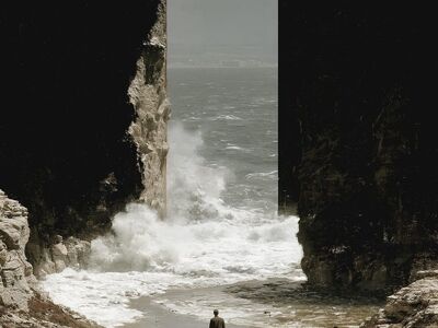seascape, coastal cliffs, crashing waves, rock formation, alone, male figure, solitude, nature, mysterious, coastal, dramatic, sunset, gateway, transition, distant view, natural archway, perspective, wild, meaningful