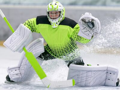 ice hockey, goalie, young athlete, protective gear, hockey stick, puck, ice rink, youth hockey, catching glove, winter sport, dynamics, neon jersey, movement, sporting event, concentration, goalie mask, goalie pads, energy