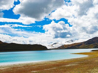 yamdrok lake, tibetan plateau, sacred lake, turquoise water, snow-capped mountains, lakeside shore, alpine grassland, blue sky, cumulus clouds, dramatic landscape, natural landscape, panorama, wild, exploration, tranquil, clean air, mountain region, vacation escape, peaceful atmosphere