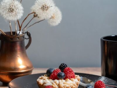 berry tarts, berry, raspberries, blueberries, blackberries, powdered sugar, black plate, coffee pot, black cup, teapot, spoon, wooden table, breakfast, dessert, pastries, vintage, still life, dried flowers, dandelions, copper vase, rustic, comfortable, food photography, close up, cute